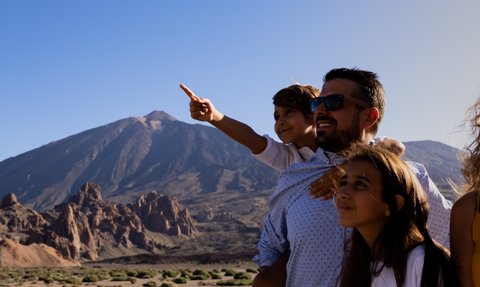 Eine Familie steht vor einer beeindruckenden Berglandschaft und zeigt auf etwas im Hintergrund, während sie lächeln.