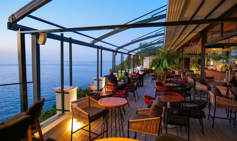 Eine stilvolle Terrasse mit Blick auf das ruhige Wasser, wo Gäste in gemütlichen Stühlen entspannen und speisen.