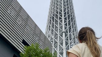 Eine Person steht vor dem Tokyo Skytree und blickt bewundernd auf den hohen Turm, umgeben von modernen Gebäuden.