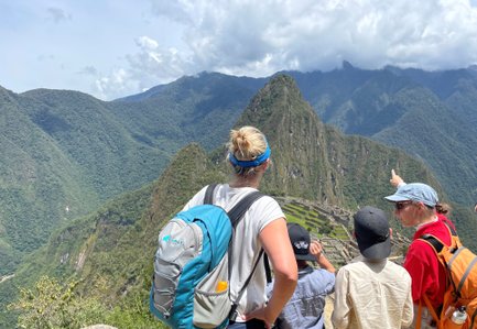 Eine Gruppe von Menschen steht auf einem Aussichtspunkt und bewundert die Ruinen von Machu Picchu inmitten der Berge.