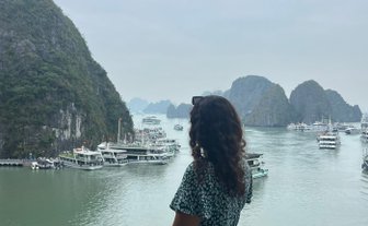 Eine Frau in einem blauen Kleid steht an einem Geländer und blickt auf die beeindruckende Halong-Bucht mit ihren Felsen.