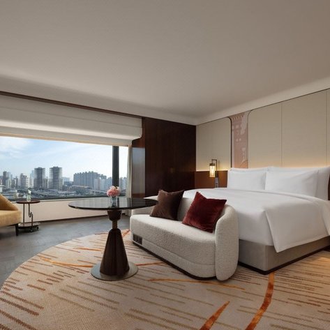 Ein modernes Hotelzimmer mit einem großen Fenster, das einen Blick auf die Stadt bietet, und eleganten Möbeln im Innenraum.