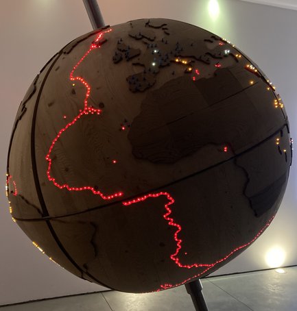 Ein beleuchteter Globus aus Holz zeigt verschiedene Kontinente mit leuchtenden Punkten in Rot und Gelb, die wichtige Orte markieren.