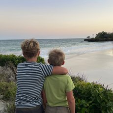 Zwei Jungen stehen am Strand, umarmt, während sie den Sonnenuntergang über dem Meer beobachten.