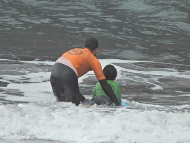 Ein Surflehrer hilft einem Kind, das im Wasser sitzt, während die Wellen sanft um sie herum plätschern.