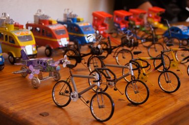 Eine Vielzahl von handgefertigten Modellfahrrädern und Spielzeugautos auf einem Holztisch, die farbenfroh und detailliert sind.