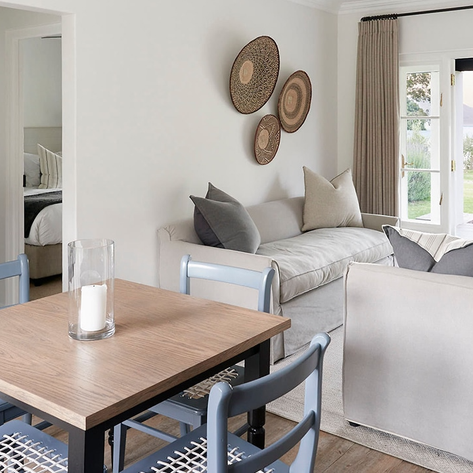 Ein helles Wohnzimmer mit einem bequemen Sofa, einem Holztisch und einem Blick auf den Garten durch große Fenster.