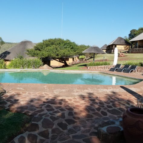 Ein einladender Pool in einem malerischen Lodge-Umfeld, umgeben von üppigem Grün und traditionellen Strohdächern.
