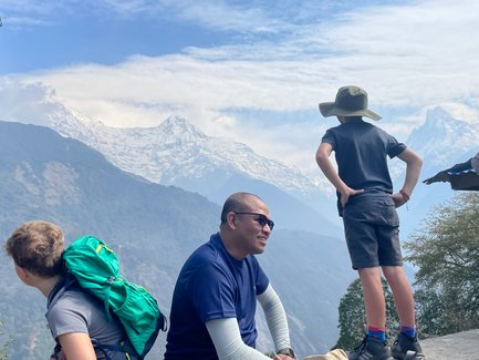 Ein Junge mit einem Hut steht nachdenklich auf einem Felsen und blickt auf die majestätischen schneebedeckten Berge.