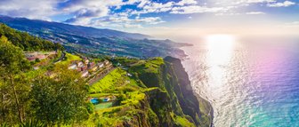 Eine atemberaubende Küstenlandschaft mit steilen Klippen, üppigem Grün und dem glitzernden Ozean im Hintergrund.