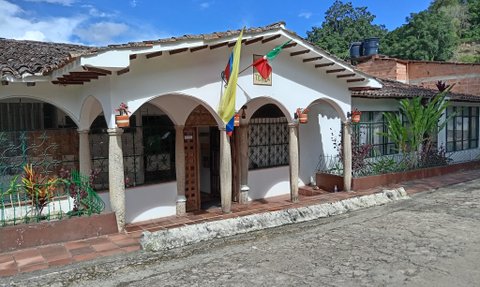 Ein charmantes Hotel mit weißen Wänden und einem traditionellen Dach, umgeben von üppigem Grün und blauen Himmel.