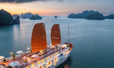 Ein traditionelles Schiff mit roten Segeln gleitet sanft über das ruhige Wasser der Halong-Bucht, umgeben von beeindruckenden Felsen.