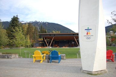 Im Vordergrund stehen bunte Adirondack-Stühle, während im Hintergrund die majestätischen Berge von Vancouver sichtbar sind.