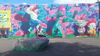 Eine Person sitzt auf einem bunten Felsen vor einer lebhaften Wandmalerei mit Cartoonfiguren in Wynwood, Miami.