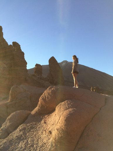 Eine Person steht auf einem großen Felsen und blickt auf die beeindruckenden Felsformationen im Hintergrund.