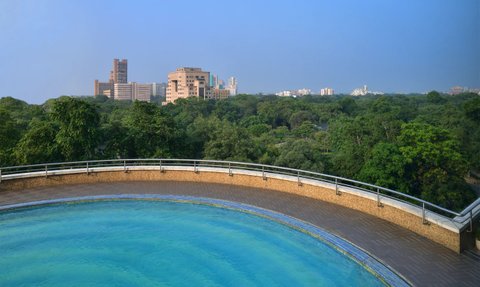 Ein atemberaubender Blick auf einen Pool mit klarem Wasser, umgeben von üppigem Grün und modernen Gebäuden im Hintergrund.