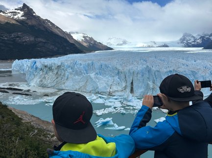 Zwei Kinder stehen an einem Aussichtspunkt und betrachten den beeindruckenden Perito-Moreno-Gletscher unter einem blauen Himmel.