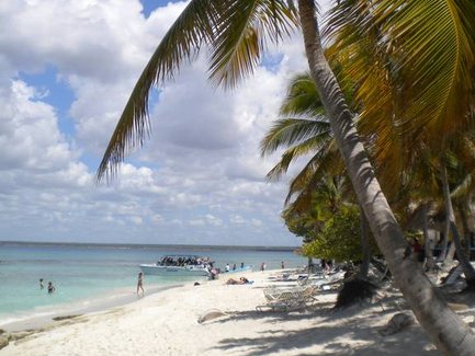Ein sonniger Strand in der Dominikanischen Republik mit Palmen, feinem Sand und Menschen, die im Wasser entspannen.