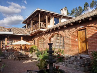 Eine charmante Hacienda mit roten Ziegelwänden, einem Innenhof und einem Brunnen, umgeben von Pflanzen und Blumen.