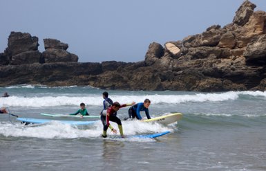 Eine Gruppe von Kindern surft fröhlich auf den Wellen des Algarve-Strandes, umgeben von beeindruckenden Felsen.