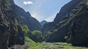 Eine beeindruckende Schlucht in den Bergen, umgeben von steilen Felsen und üppigem Grün, unter einem klaren blauen Himmel.