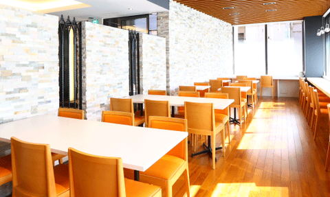 Ein modernes Restaurant mit hellen Holzböden und orangefarbenen Stühlen, das eine einladende Atmosphäre ausstrahlt.