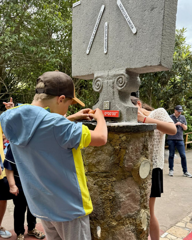 Ein Junge und ein Mädchen stehen an einem monumentalen Stein, der den Äquator markiert, und untersuchen die Inschriften.