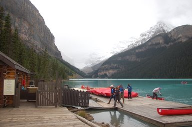 Am Ufer des Maligne Lake stehen Menschen, während Kanus auf dem ruhigen, türkisfarbenen Wasser schwimmen.