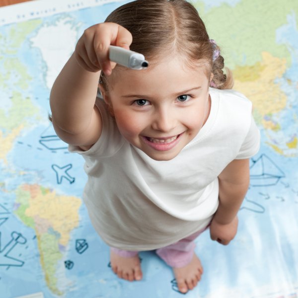 Ein fröhliches Mädchen steht auf einer Weltkarte und hält einen Marker, bereit, etwas zu zeichnen oder zu markieren.