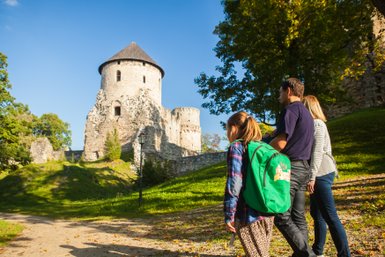 Eine Familie erkundet die beeindruckende Festung Cesis, umgeben von üppigem Grün und klarem Himmel.