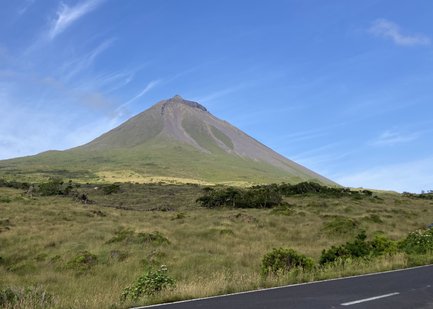 Ein majestätischer Vulkan erhebt sich über eine grüne Landschaft unter einem klaren blauen Himmel.