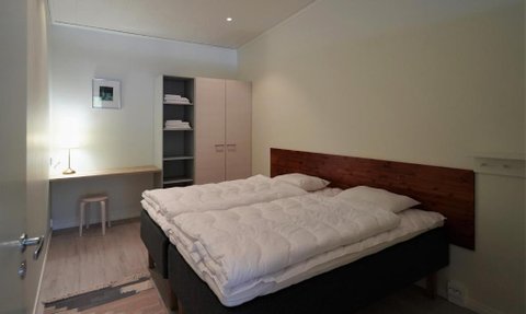 Ein gemütliches Schlafzimmer mit einem großen Doppelbett, einem Schreibtisch und einem Stuhl in sanften Farben.