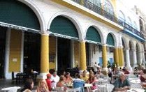 Eine belebte Restaurantterrasse mit Gästen, die an Tischen sitzen und die Atmosphäre genießen, umgeben von bunten Gebäuden.