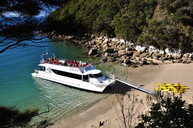 Ein Wassertaxi liegt an einem Sandstrand, während Passagiere an Bord die Aussicht auf das klare Wasser genießen.