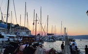 Ein malerischer Hafen mit vielen Segelbooten, während die Sonne hinter den Bergen untergeht und den Himmel in sanften Farben färbt.