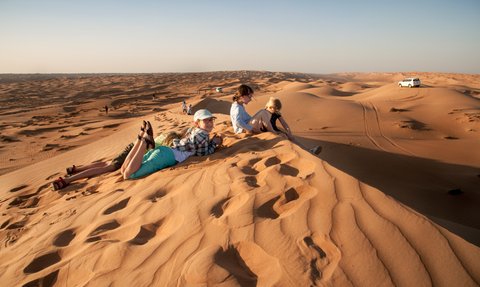 Kinder sitzen gemeinsam auf einer Wüstendüne – Oman Familienreise