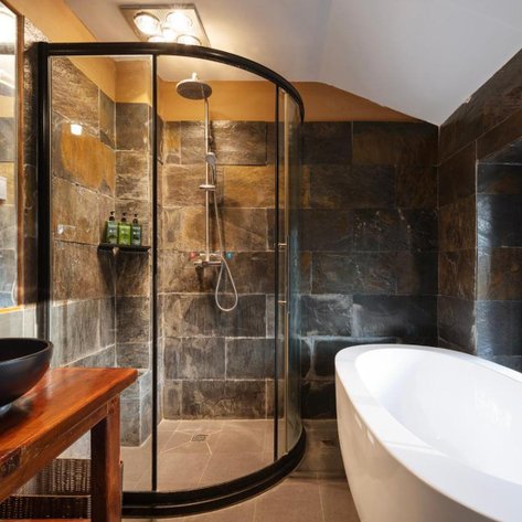 Ein modernes Badezimmer mit einer eleganten Badewanne und einer gläsernen Dusche, umgeben von stilvollen Steinfliesen.