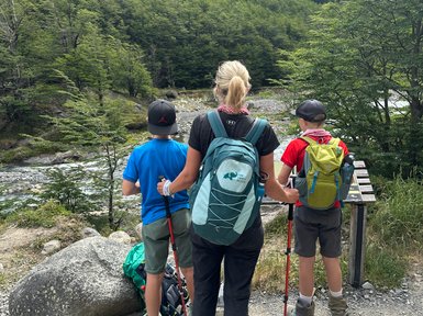 Eine Frau steht mit zwei Kindern am Wanderweg und blickt auf die beeindruckenden Berge im Hintergrund.