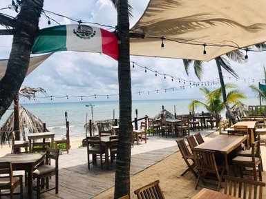 Ein einladendes Restaurant am Strand mit Holztischen und Stühlen, umgeben von Palmen und einer sanften Meeresbrise.