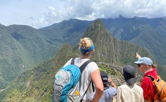 Eine Gruppe von Menschen steht auf einem Aussichtspunkt und bewundert die Ruinen von Machu Picchu inmitten der Berge.