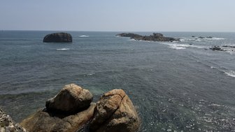 Eine ruhige Küstenlandschaft mit großen Felsen, die im klaren Wasser stehen, während sanfte Wellen an die Küste schlagen.