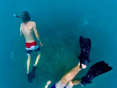 Zwei Schnorchler schwimmen im klaren Wasser, umgeben von Unterwasserfelsen und Sand, während das Licht schimmert.