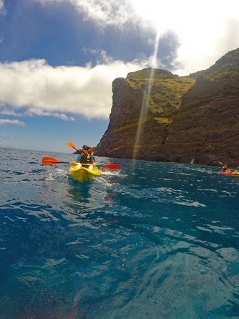 Zwei Kajakfahrer paddeln in klarem Wasser vor einer beeindruckenden Felsenküste unter einem strahlend blauen Himmel.