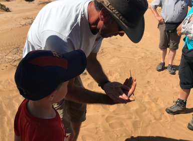 Ein Mann und ein Kind beobachten eine Echse - Namibia mit Jugendlichen