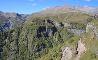 Eine atemberaubende Berglandschaft mit sanften Hügeln und steilen Klippen, umgeben von üppigem Grün und klarem blauen Himmel.