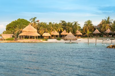 Ein ruhiger Strand mit mehreren Strohhütten, umgeben von üppigen Palmen und klarem Wasser, ideal für Entspannung.