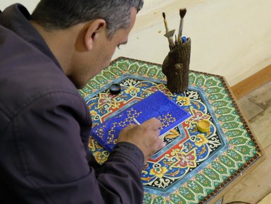 Ein Künstler konzentriert sich auf die Miniaturmalerei, während er feine Details auf einer blauen Fläche hinzufügt.