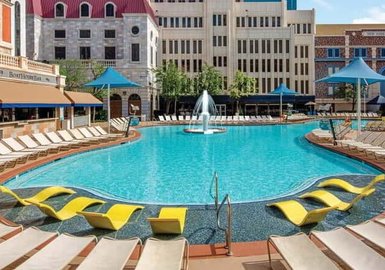 Ein einladender Pool mit klarem Wasser, umgeben von gelben Liegen und schattenspendenden Sonnenschirmen in einer urbanen Umgebung.