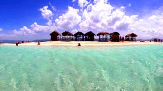 Eine malerische Insel mit klarblauem Wasser und strohgedeckten Hütten, umgeben von sanften Wellen und strahlendem Himmel.