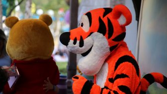 Ein fröhlicher Tigerkostümträger lächelt, während er neben einem gelben Bären steht, der den Rücken zur Kamera hat.